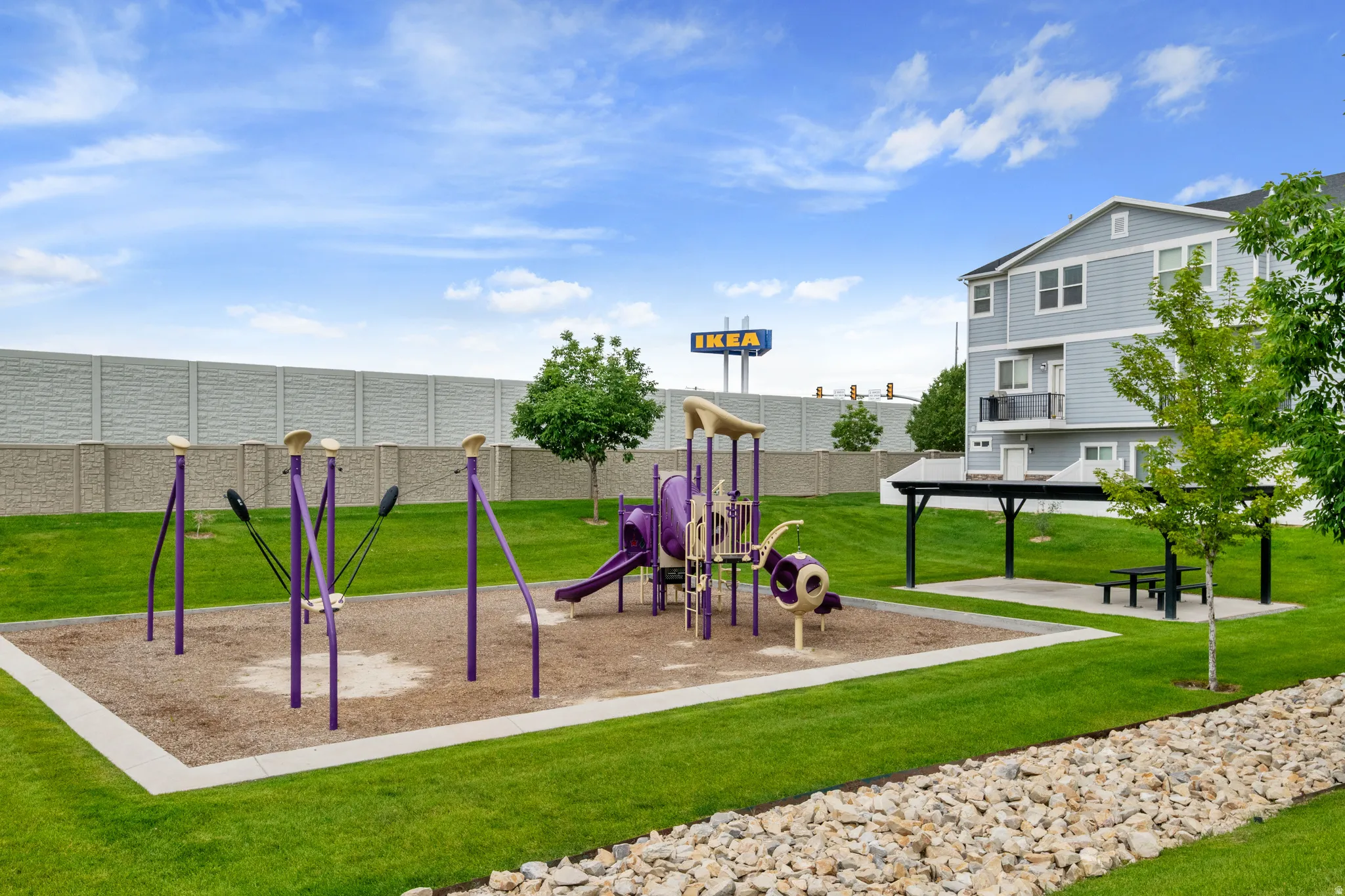 Community playground featuring purple and beige play structures on a sand base, surrounded by manicured green lawns
