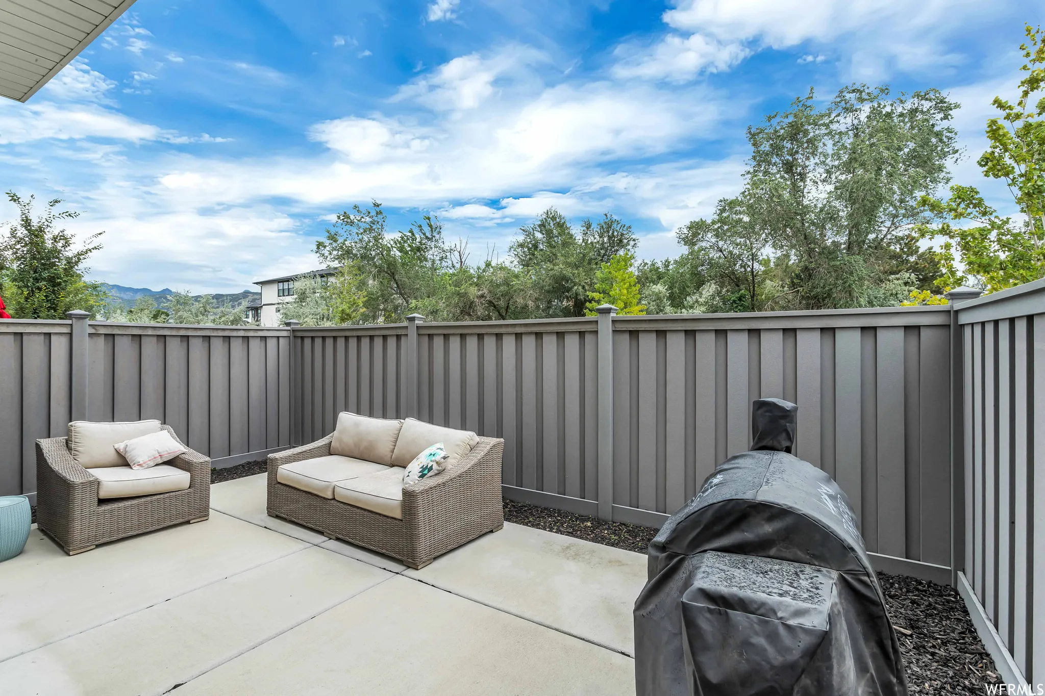 Private patio space featuring a concrete pad, dark gray privacy fencing, and dark gravel landscaping