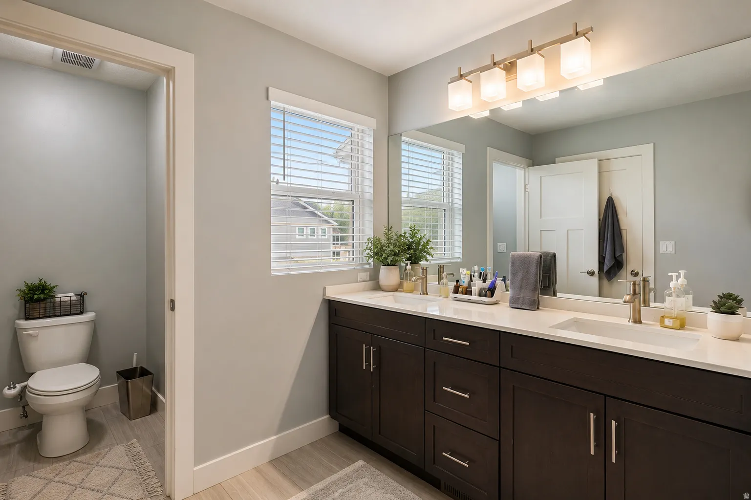 Bathroom featuring a dual vanity with dark wood cabinetry and light countertops, two rectangular undermount sinks, and two windows with horizontal blinds