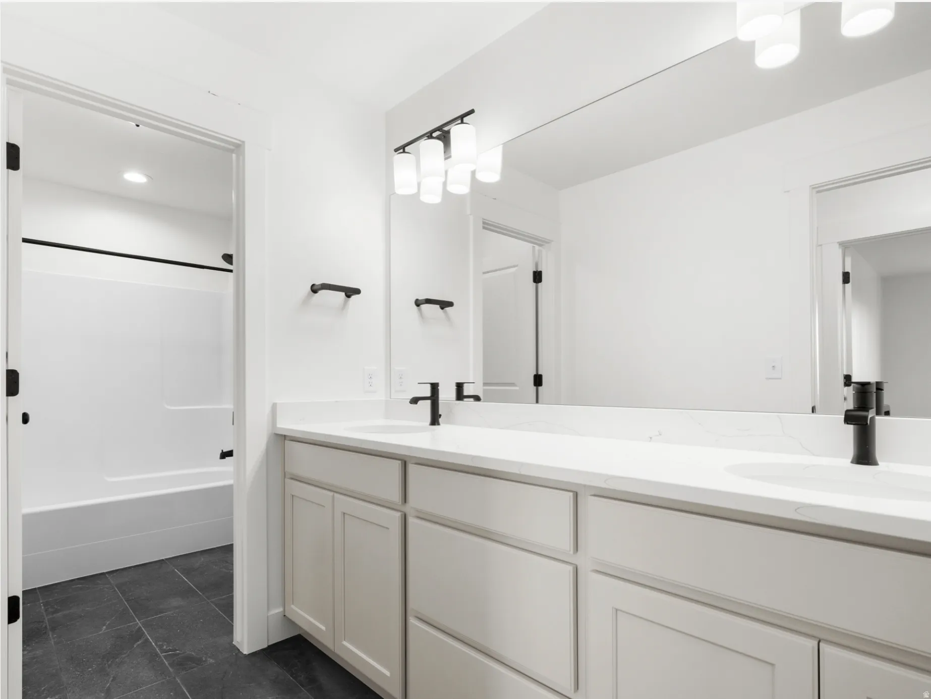 Bathroom featuring a double vanity with light-toned cabinetry, white countertops, and black fixtures