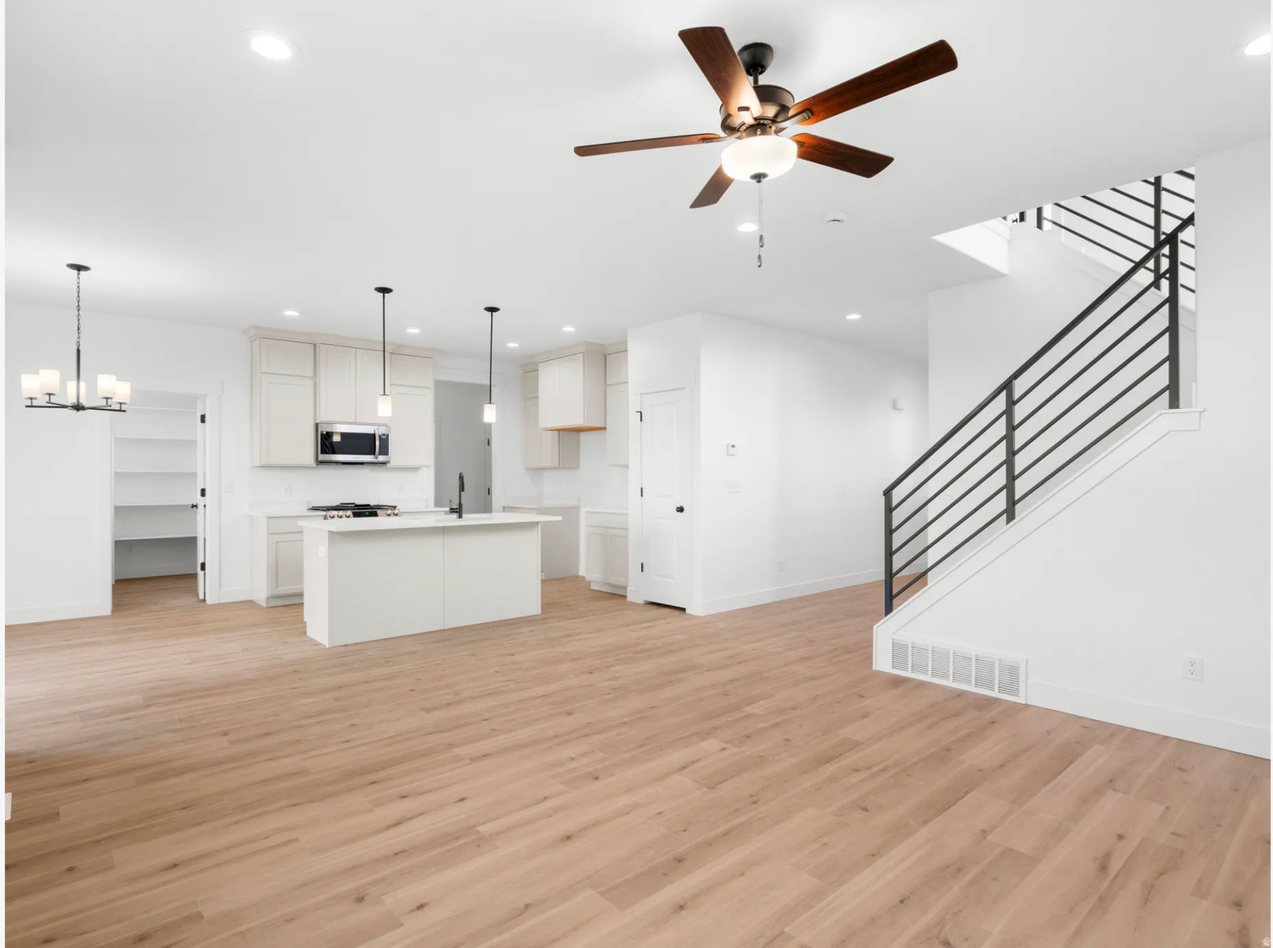Open-concept living space with wood-finish flooring, a contemporary kitchen, a kitchen island, a pantry, and a modern staircase with metal railings