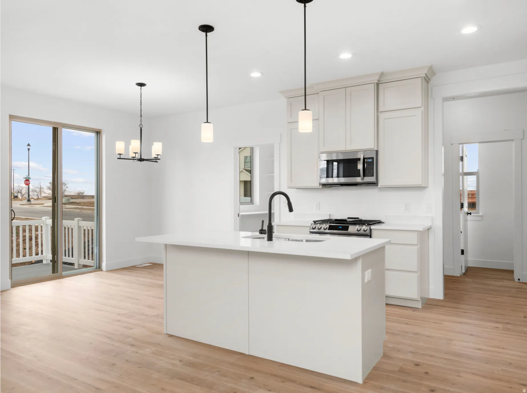 Contemporary kitchen featuring a center island with sink, white cabinetry, stainless steel appliances, and wood-finish flooring