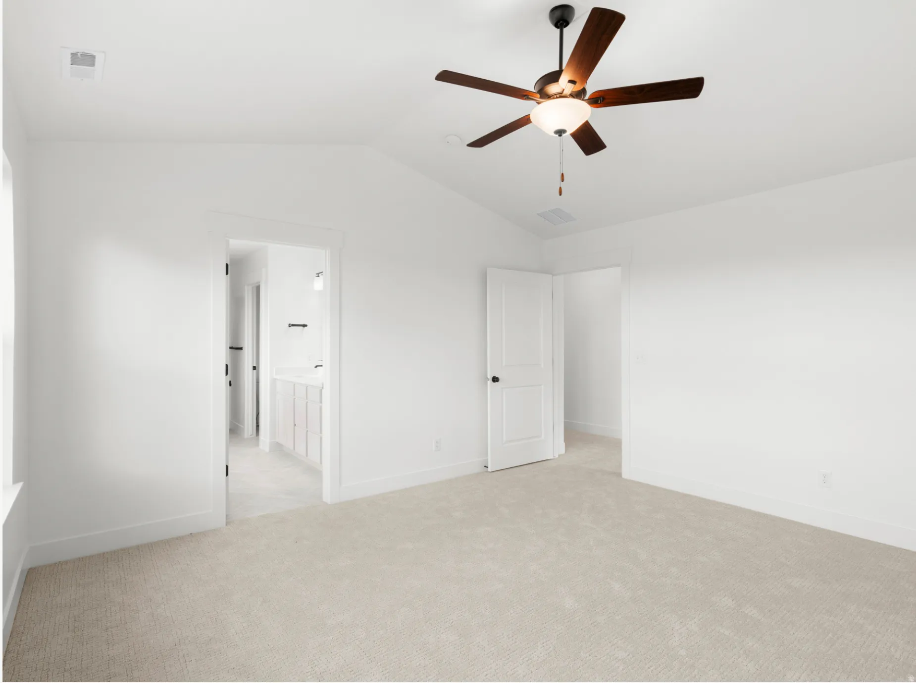 Vaulted ceiling room featuring light-toned carpeting, a ceiling fan with dark wood-finish blades, and a white paneled door