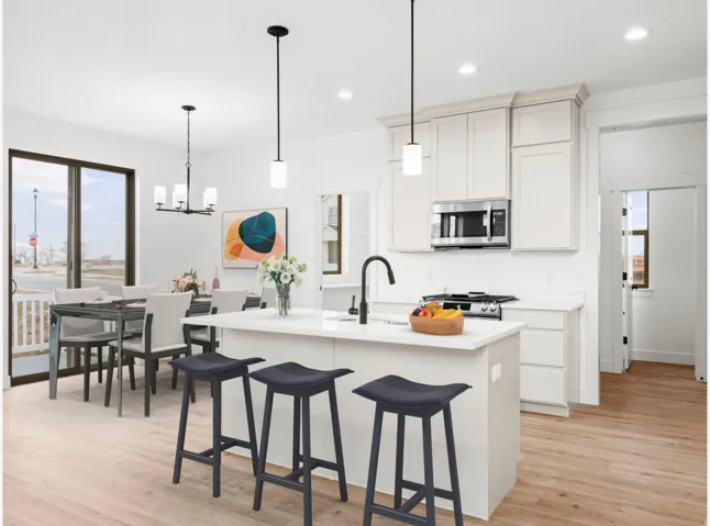 Open-concept kitchen and dining area featuring light wood-finish flooring, white cabinetry, a central island with a sink and black faucet, and stainless steel appliances