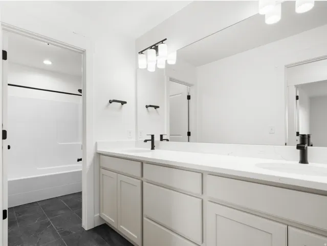 Bathroom featuring a double vanity with light-toned cabinetry, white countertops, and black fixtures