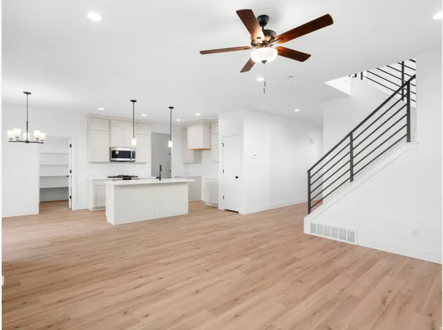 Open-concept living space with wood-finish flooring, a contemporary kitchen, a kitchen island, a pantry, and a modern staircase with metal railings