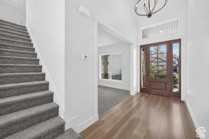Entryway featuring wood-finish flooring, a wood-panel front door with glass inserts and sidelights, and a high ceiling with a contemporary chandelier
