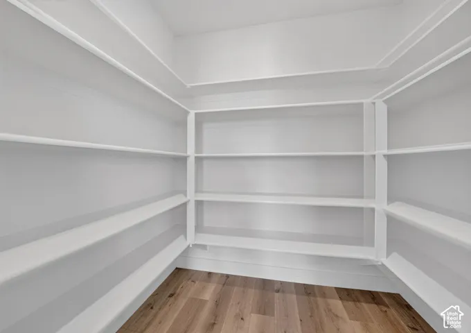 Walk-in pantry featuring expansive shelving, white painted walls, white baseboards, and wood-finish flooring
