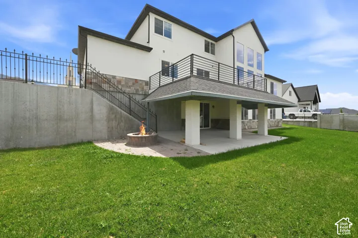 Expansive rear elevation featuring a covered patio, upper-level balcony with black railing, and a stone fire pit