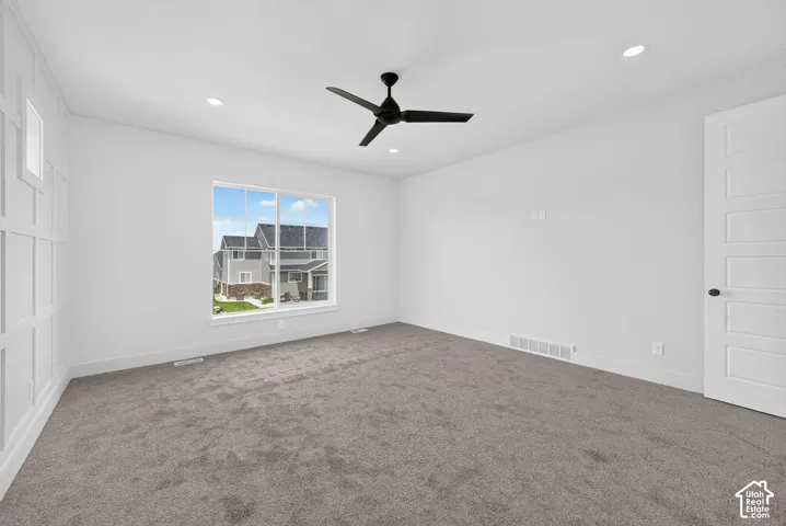 Carpeted room featuring a large window, a black ceiling fan, recessed lighting, and a paneled accent wall
