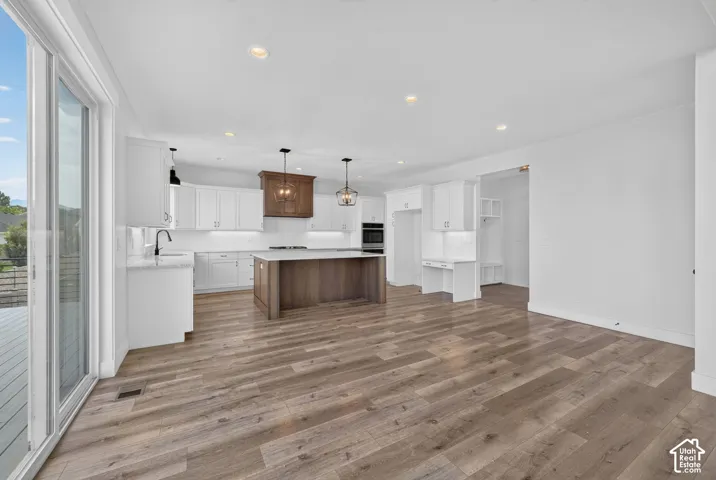 Open-concept kitchen featuring white cabinetry, a large wood-finish island with a stone countertop, and wood-finish flooring