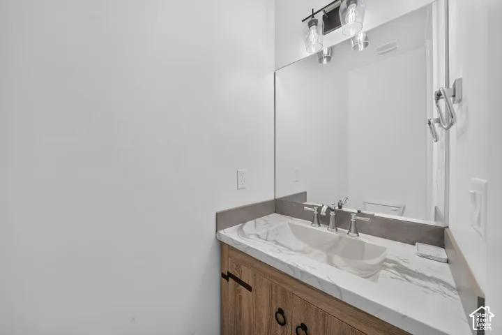 Bathroom vanity featuring a vessel sink, marble-finish countertop, brushed nickel faucet, and wood-finish cabinetry with dark hardware