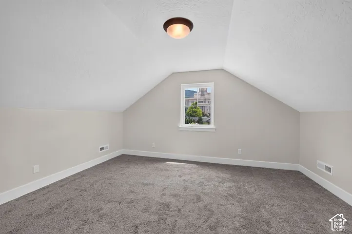 Carpeted room featuring sloped ceilings and a single window with white trim