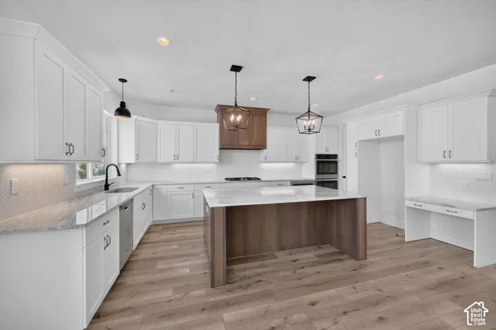 Spacious kitchen featuring an expansive island with a stone-finish countertop, white cabinetry, wood-finish flooring, and built-in double ovens