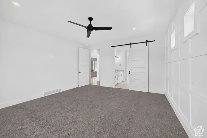 Spacious room featuring a decorative accent wall with recessed square panels, dark gray carpeting, and a modern black ceiling fan