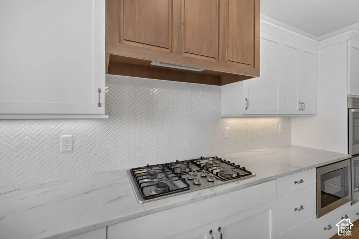 Gourmet kitchen featuring a built-in gas range, white shaker cabinetry, herringbone tile backsplash, and light-toned countertops