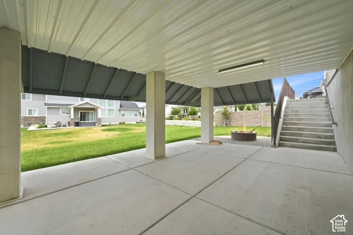 Covered patio with concrete flooring, supported by square pillars, featuring a metal fire pit and exterior staircase with handrails