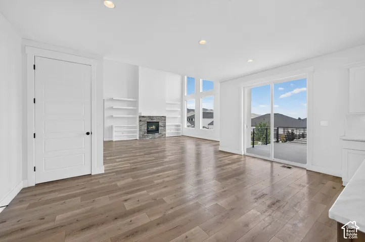 Open-concept living area featuring wood-finish flooring, a stone-clad fireplace, and expansive windows