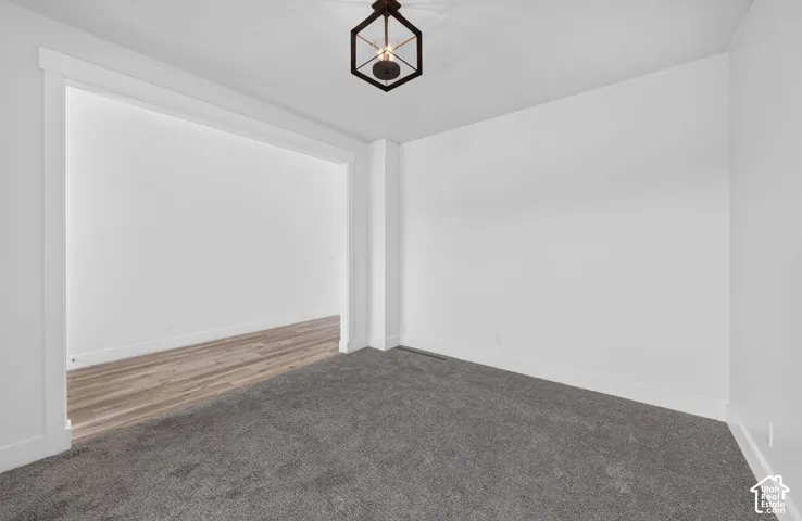 Spacious room featuring plush gray carpeting, white walls, white baseboards, and a modern geometric ceiling light fixture