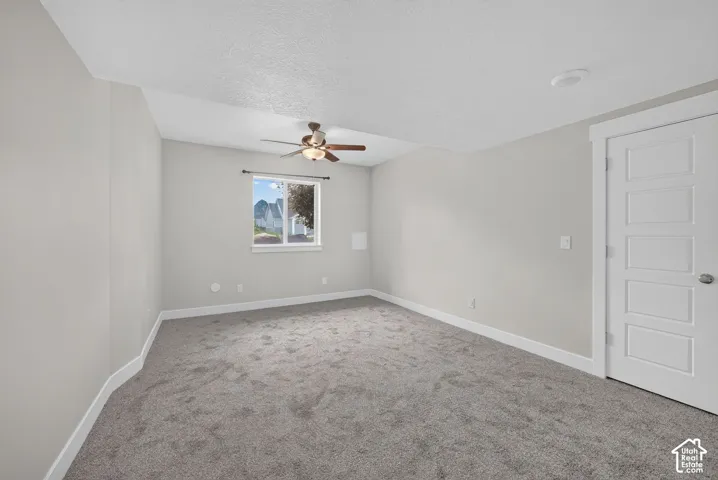 Spacious room featuring gray carpet, light gray walls, a window with white trim, a ceiling fan, and a contemporary five-panel door