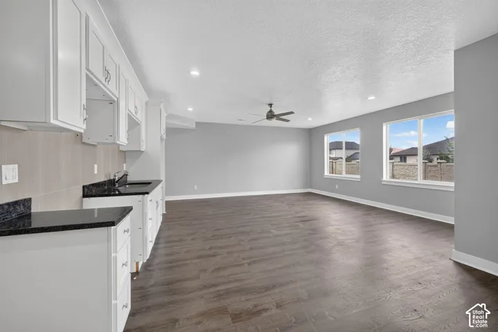 Spacious open-concept area featuring white cabinetry, dark countertops, and wood-finish flooring