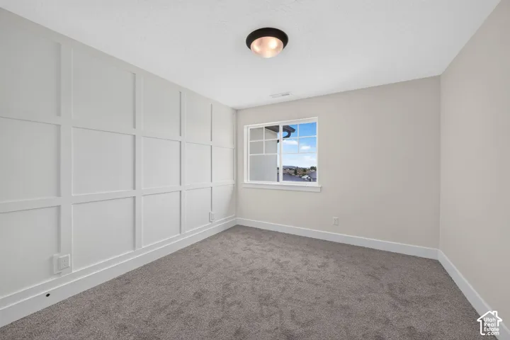 Interior room featuring wainscoting accent wall, neutral carpeting, window with grid panes, and flush-mount ceiling light