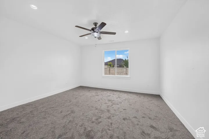Spacious room featuring neutral carpeting, white walls, a single window, recessed lighting, and a ceiling fan