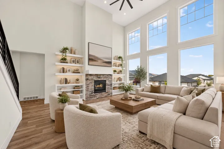 Vaulted ceilings with a ceiling fan, stone-surround fireplace, built-in shelving, wood-finish flooring, and large windows