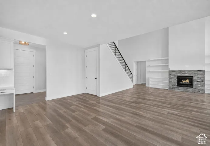 Spacious living area featuring wood-finish flooring, a stone-accented fireplace, and built-in shelving