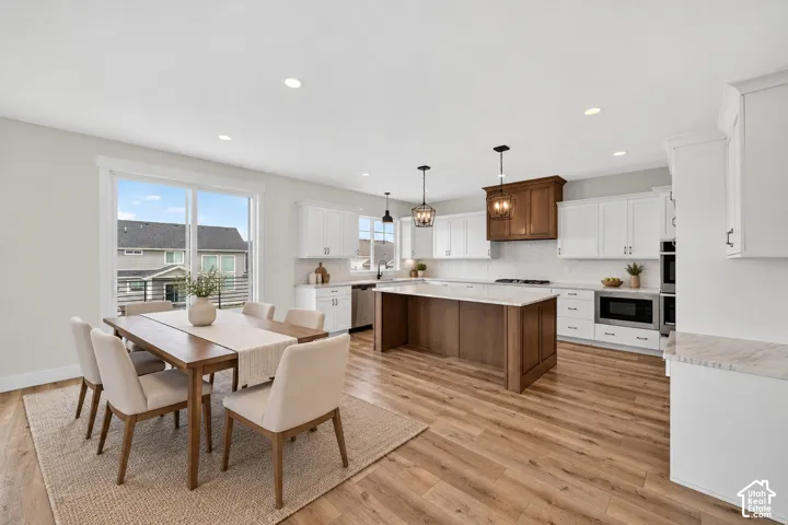 Open-concept kitchen and dining area featuring wood-finish flooring, white cabinetry, a kitchen island with stone countertops, stainless steel appliances, and recessed lighting