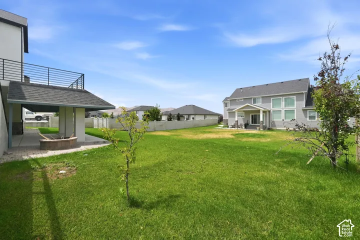 Expansive grassy yard featuring a covered patio, built-in fire pit, and a second-story balcony with metal railing