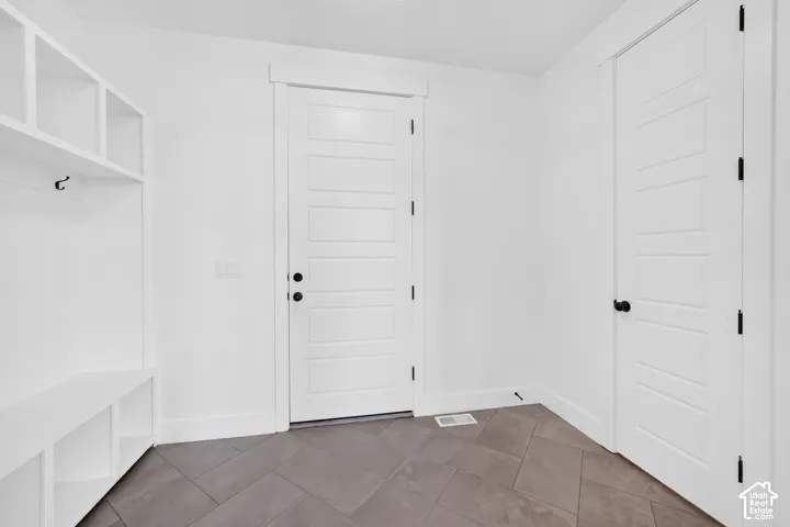 Built-in white storage bench with cubbies and hooks, complemented by a large white five-panel interior door with black hardware, and dark gray flooring laid in a herringbone pattern