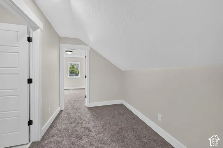 Open doorway framing a window with outdoor scenery, neutral wall tones, white trim, gray textured carpeting, and a white paneled door