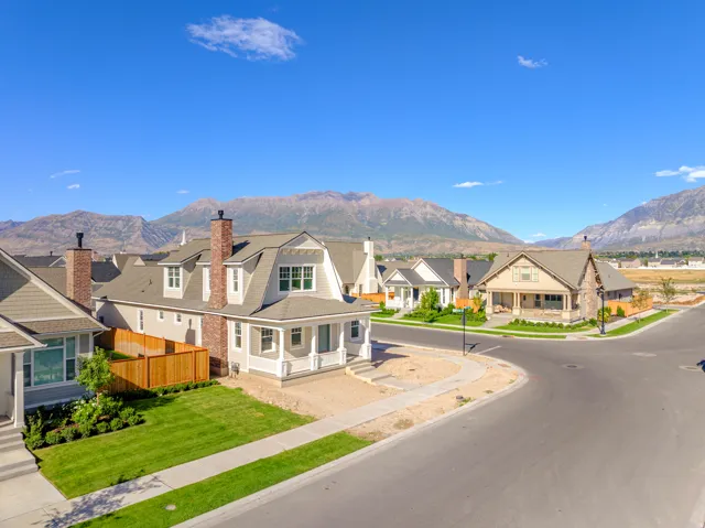 Modern residential architecture featuring dormer windows, brick chimneys, a covered front porch, and a manicured lawn