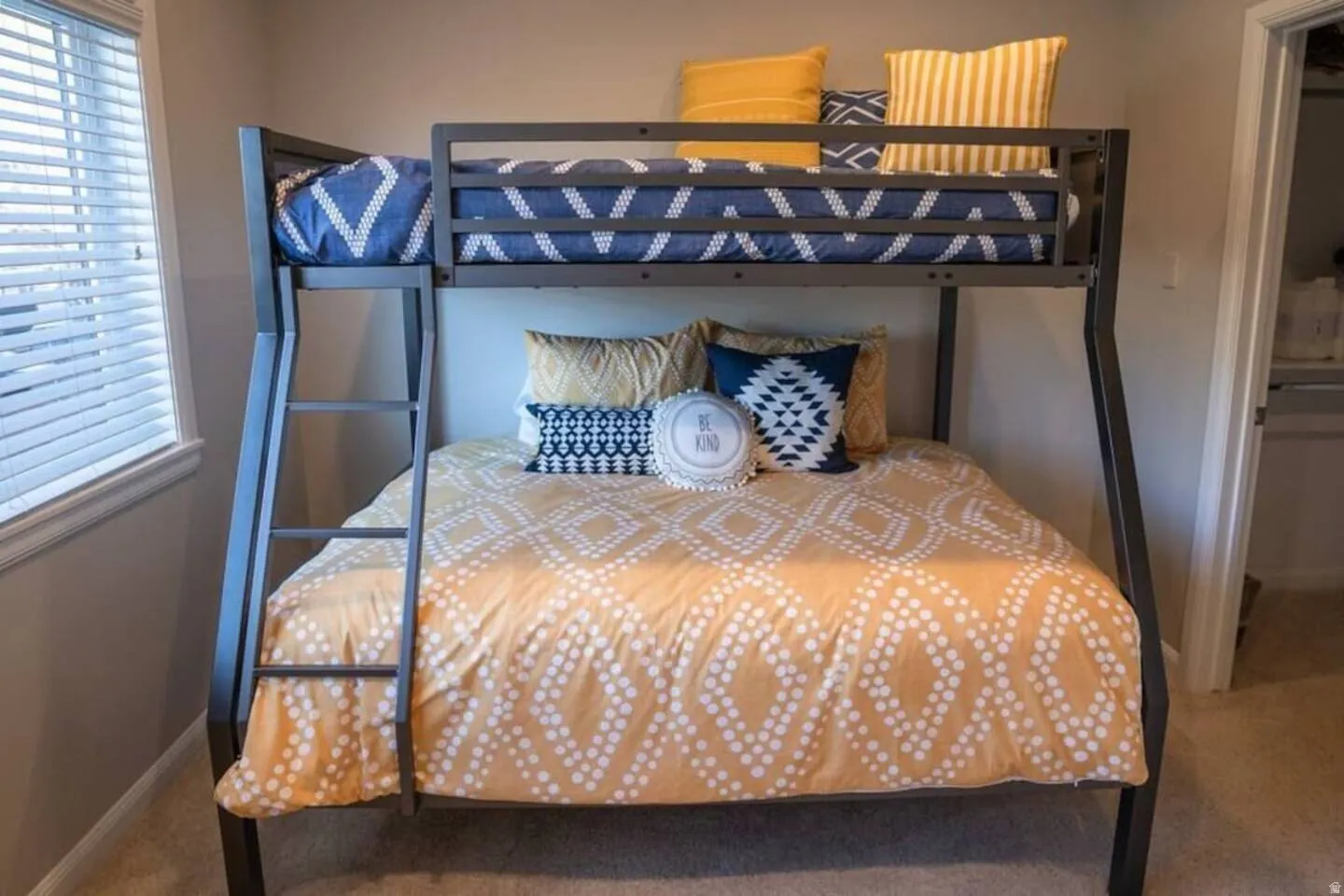 Bedroom featuring a metal bunk bed frame with integrated ladder, a window with horizontal blinds, neutral wall paint, and carpet flooring