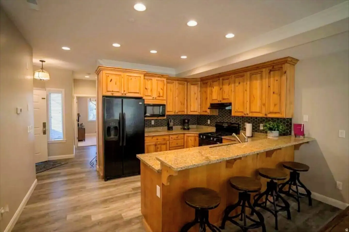 Kitchen featuring light wood cabinetry, granite-finish countertops, black appliances, and a tiled backsplash