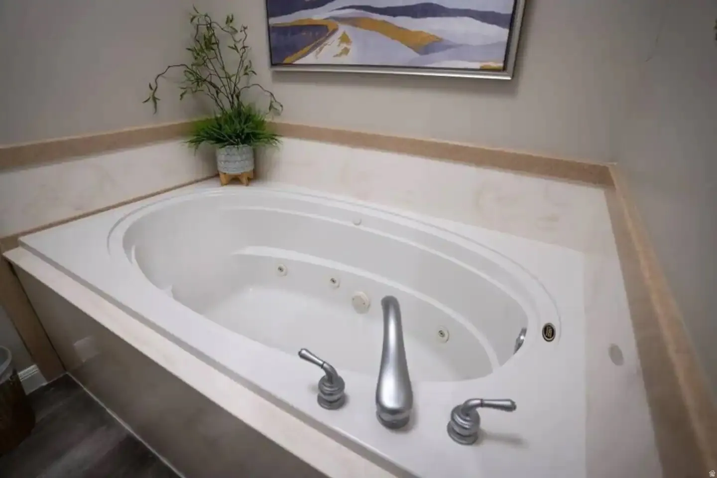 Corner jetted bathtub with a white finish, featuring a built-in deck with a light-toned countertop and coordinating wall trim