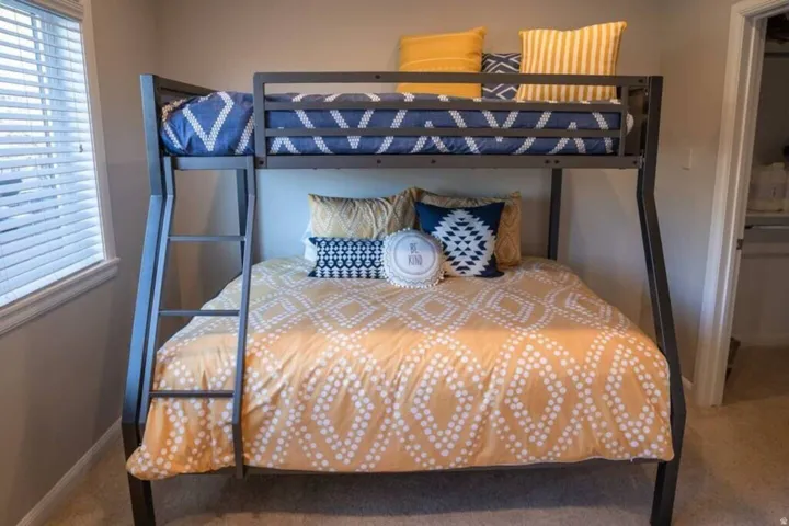 Bedroom featuring a metal bunk bed frame with integrated ladder, a window with horizontal blinds, neutral wall paint, and carpet flooring