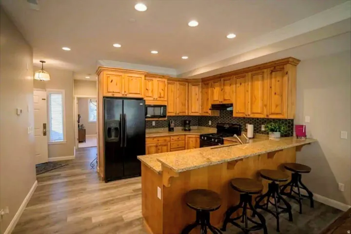 Kitchen featuring light wood cabinetry, granite-finish countertops, black appliances, and a tiled backsplash