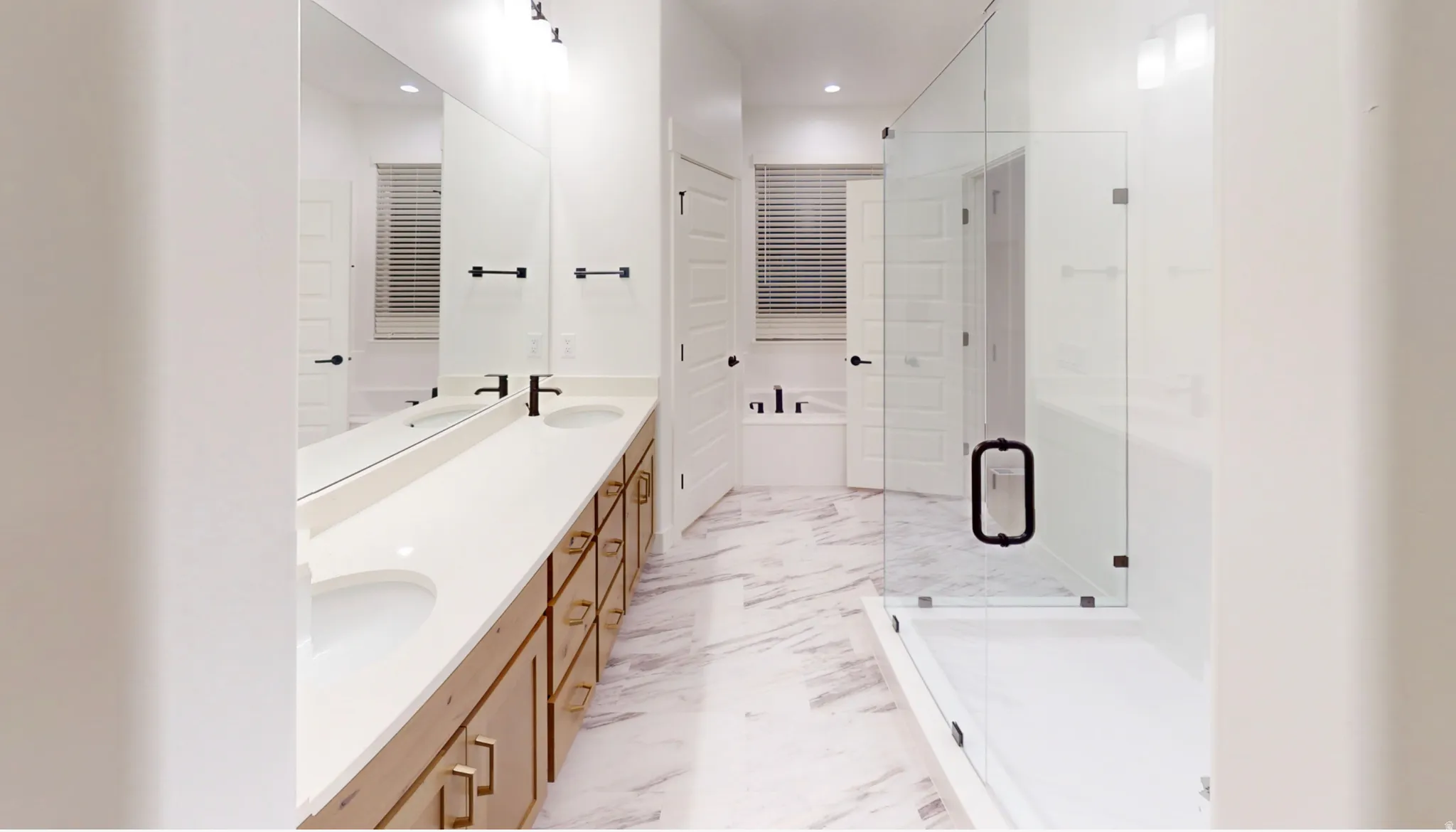 Spacious bathroom featuring a dual vanity with light wood-finish cabinetry, white countertops, and matte black fixtures