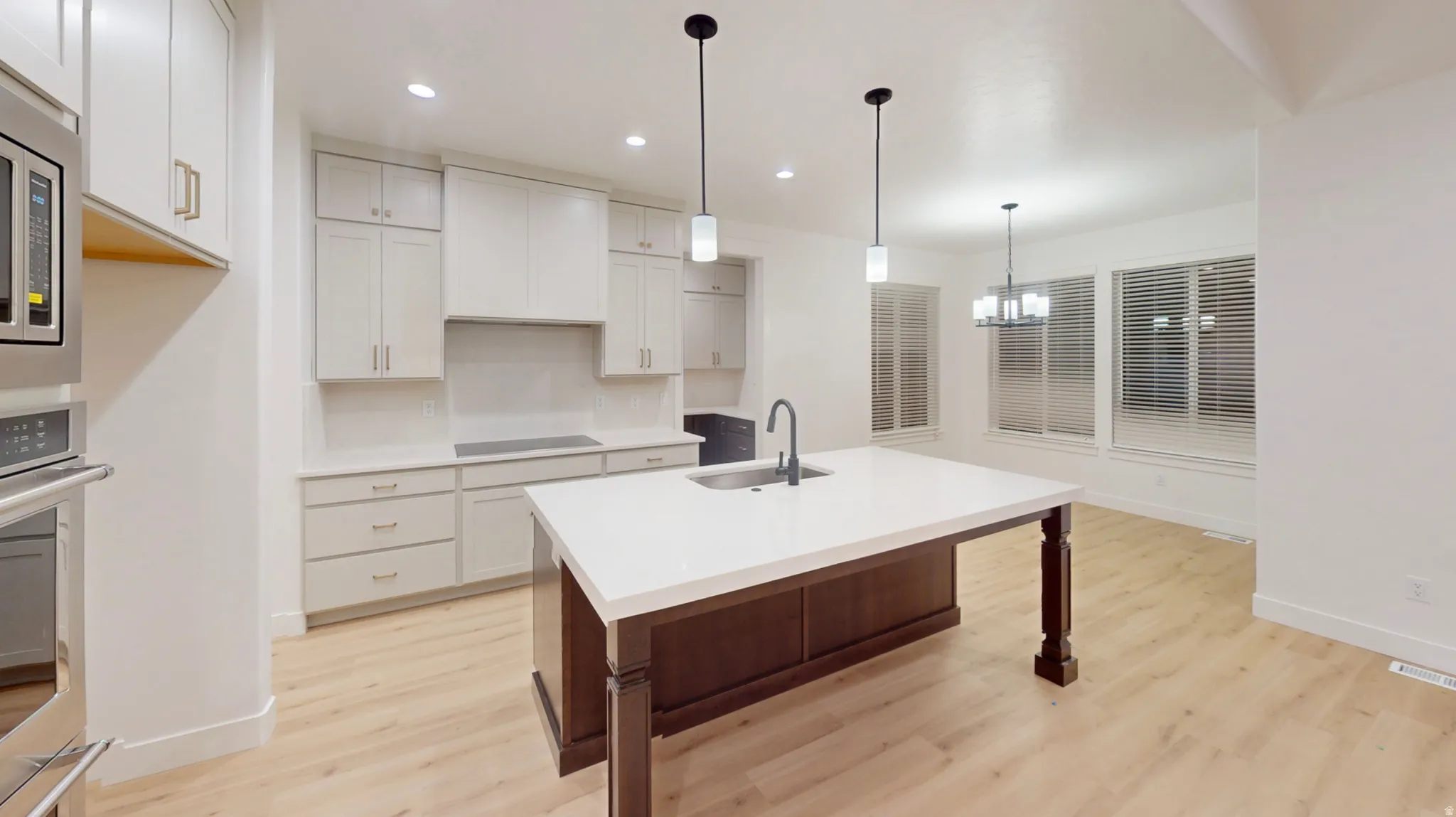 Kitchen featuring a large island with a white countertop and dark wood base, light wood-finish flooring, white cabinetry, stainless steel appliances, and pendant lighting