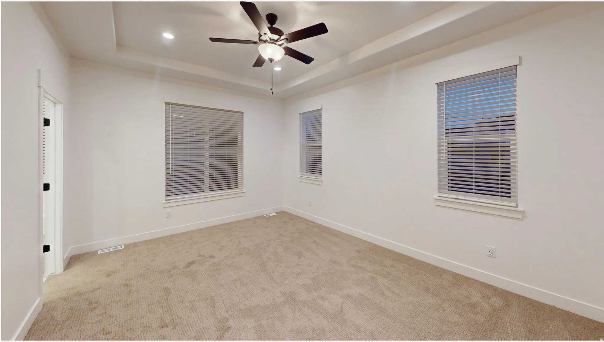 Light-filled interior featuring a tray ceiling, recessed lighting, ceiling fan, and carpeted flooring
