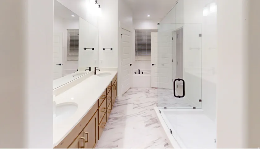 Spacious bathroom featuring a dual vanity with light wood-finish cabinetry, white countertops, and matte black fixtures