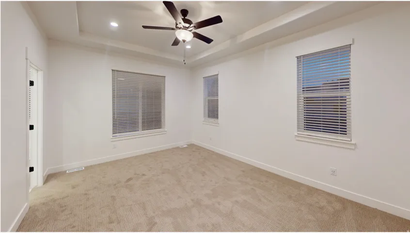 Light-filled interior featuring a tray ceiling, recessed lighting, ceiling fan, and carpeted flooring