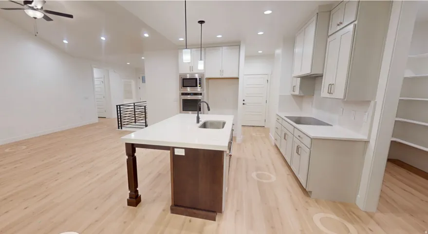 Contemporary kitchen featuring a substantial island with integrated sink, light-toned wood-finish flooring, white cabinetry, recessed lighting, and a built-in wall oven and microwave