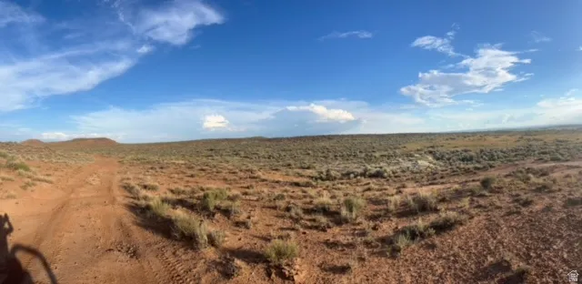 Expansive desert landscape featuring a dirt path, arid vegetation, and distant hills under a clear blue sky