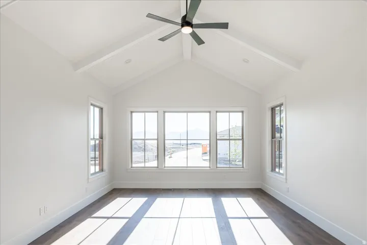Vaulted white ceiling with exposed beams, dark wood-finish flooring, and multiple windows providing ample light