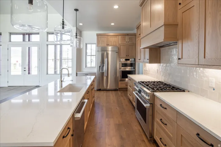 Gourmet kitchen featuring a large central island with an integrated sink, light wood-finish cabinetry, stainless steel appliances, and wood-finish flooring