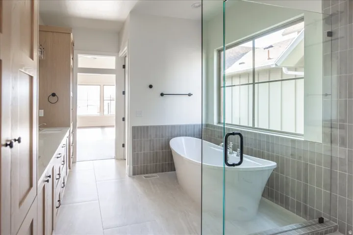 Freestanding soaking tub within a glass-enclosed shower featuring gray vertical tile work