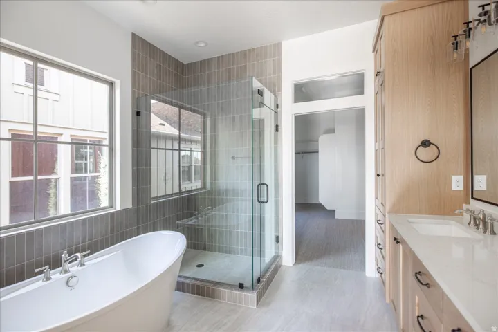 Bathroom featuring a freestanding bathtub, glass-enclosed shower with tiled walls, and a light wood-finish double vanity